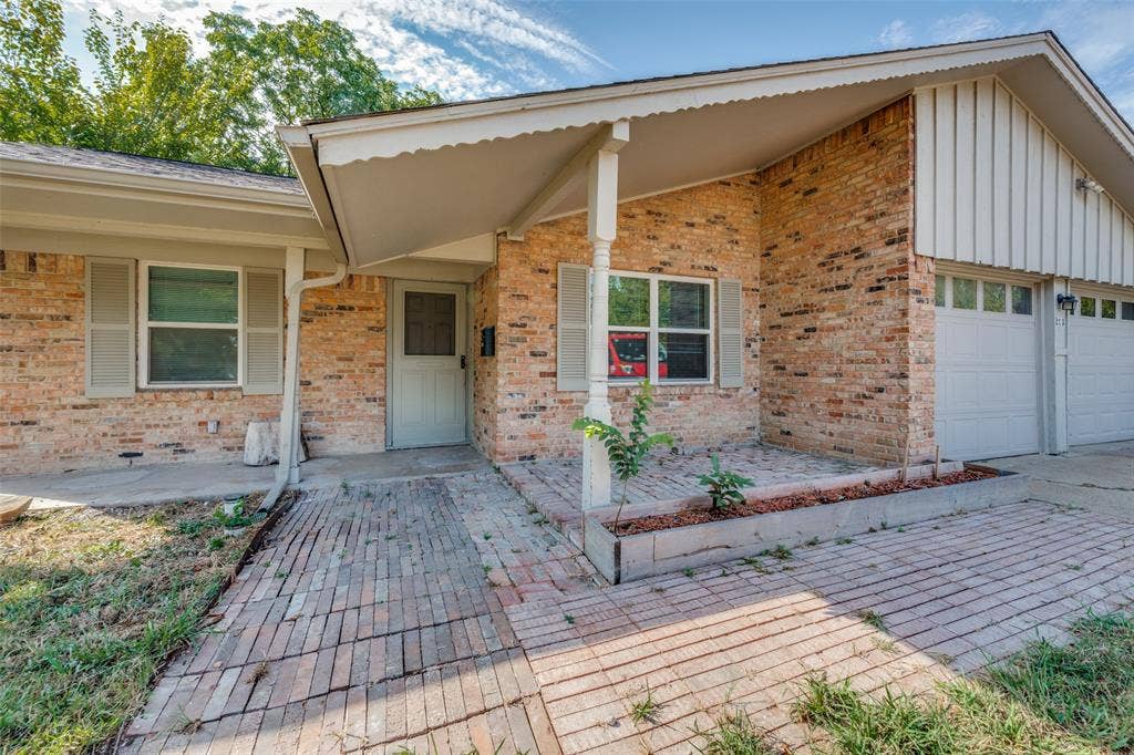 213 W Dorris Drive, Grand Prairie, TX 75051 Brick exterior with white trim, covered front entry, attached two-car garage, and a brick paver pathway