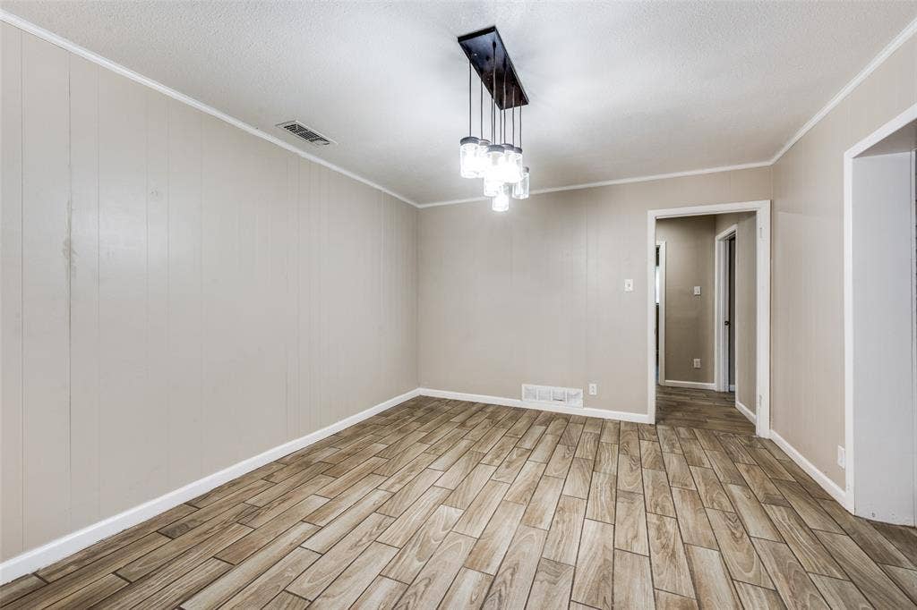 213 W Dorris Drive, Grand Prairie, TX 75051 Neutral wall paneling, wood-finish flooring, and a modern linear chandelier with glass shades