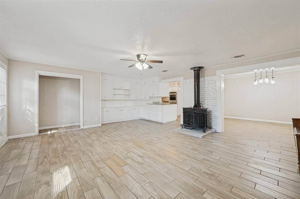 213 W Dorris Drive, Grand Prairie, TX 75051 Wood-finish tile flooring throughout, white cabinetry with built-in shelving, stove-style fireplace with white brick surround, and a ceiling fan