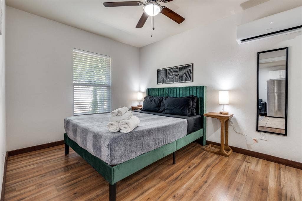 1816 Boyd Street, Dallas, TX 75224 ADU- Wood-finish flooring, ceiling fan, window with blinds, wall-mounted air conditioning unit, and a rectangular wall mirror