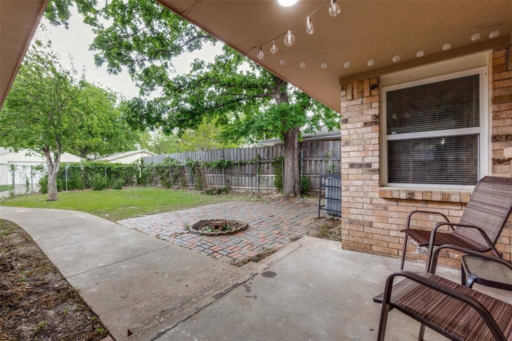 1816 Boyd Street, Dallas, TX 75224 Covered patio with concrete flooring, brick exterior, and a paver-stone fire pit area, surrounded by a wood privacy fence and mature trees