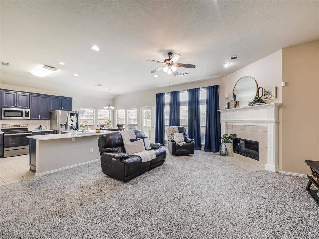 8374 Cain River Drive, Frisco, TX 75035 Open living area features a fireplace with a decorative mantel, tall windows, and easy connection to the kitchen for everyday living and entertaining.