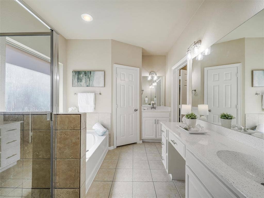8374 Cain River Drive, Frisco, TX 75035 Primary bathroom features two vanity areas, a separate glass-enclosed shower, a soaking tub, and tile flooring.