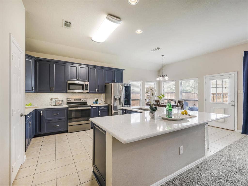8374 Cain River Drive, Frisco, TX 75035 Updated kitchen showcases deep blue cabinetry, quartz countertops, stainless steel appliances, and a generous peninsula overlooking the living room.