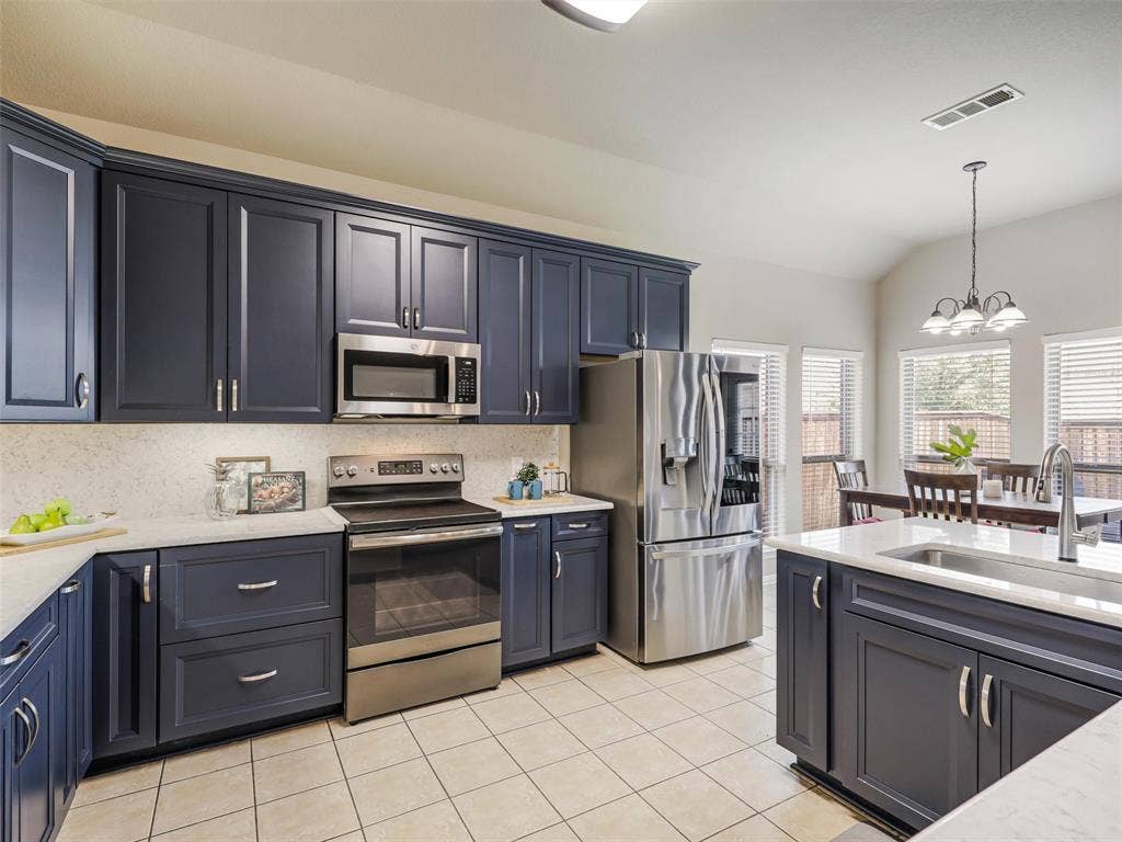 8374 Cain River Drive, Frisco, TX 75035 Updated kitchen pairs deep blue cabinetry with light countertops and backsplash, stainless steel appliances, and an adjoining breakfast area.