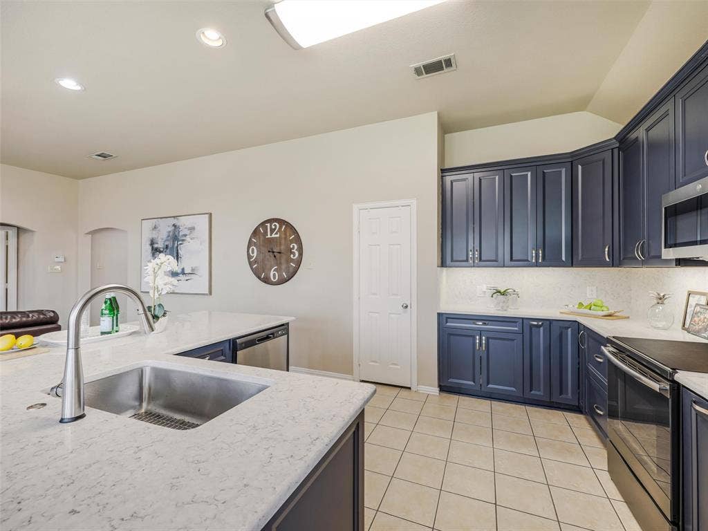 8374 Cain River Drive, Frisco, TX 75035 Kitchen features include a stainless steel undermount sink, high-arc faucet, light countertops, blue cabinetry, and a pantry for additional storage.
