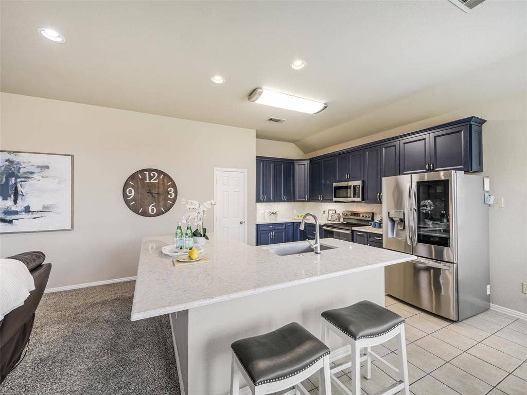 8374 Cain River Drive, Frisco, TX 75035 Expansive peninsula offers ample prep space and casual seating, complemented by blue cabinetry, stainless steel appliances, and tile flooring.