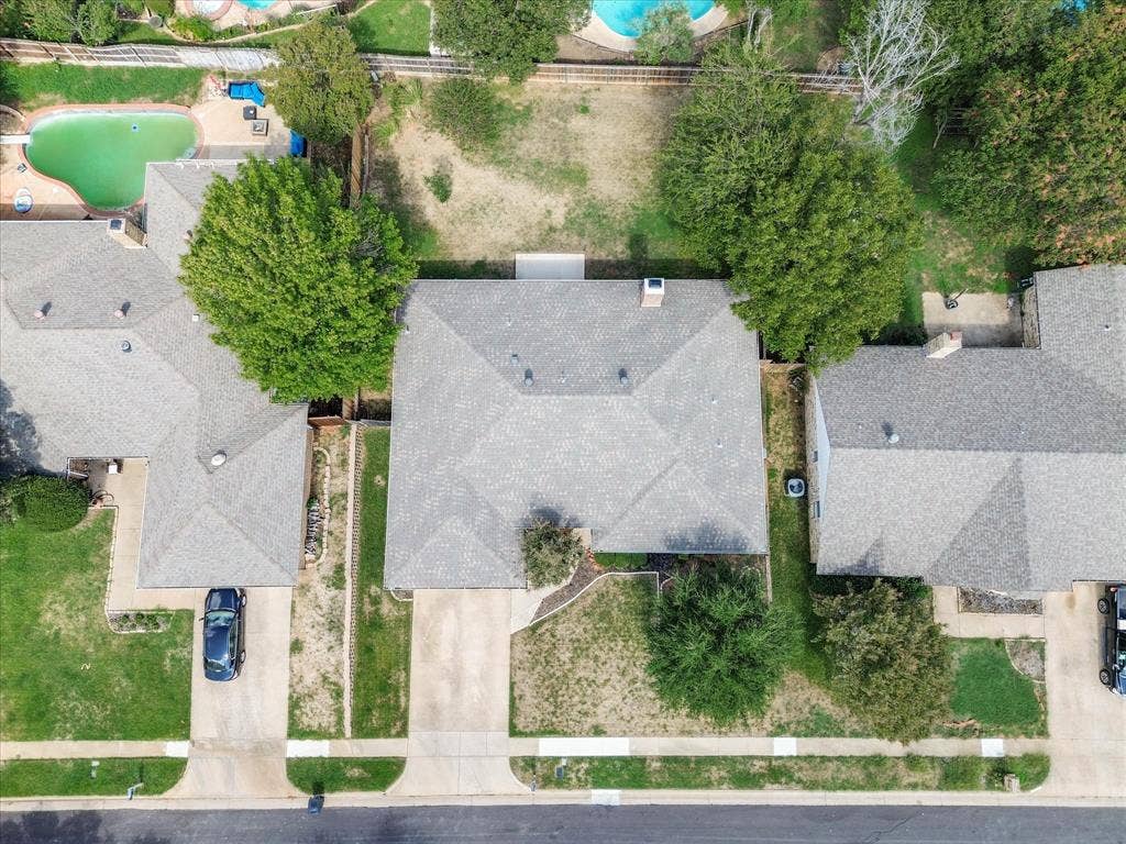 Aerial perspective of a residential lot featuring a concrete driveway, multi-faceted shingle roofline, and mature landscaping