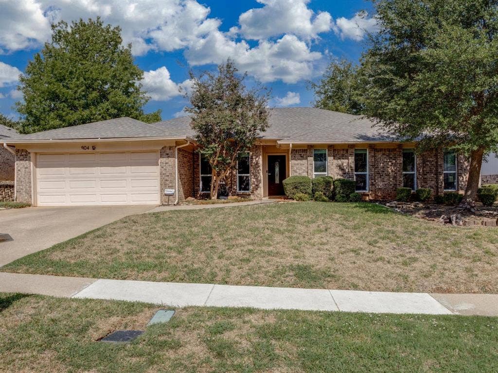 Single-story brick exterior featuring a multi-gabled roofline, an attached two-car garage, and established landscaping