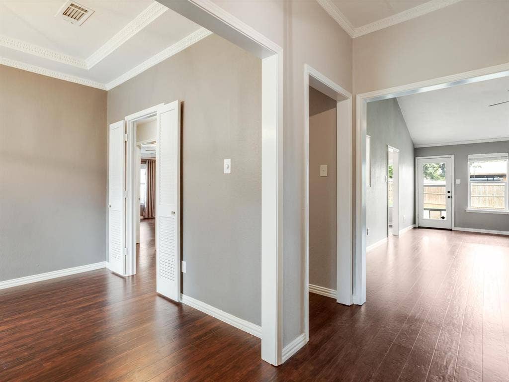 Interior featuring wood-finish flooring, crisp crown molding, recessed tray ceiling detailing, and white louvered closet doors