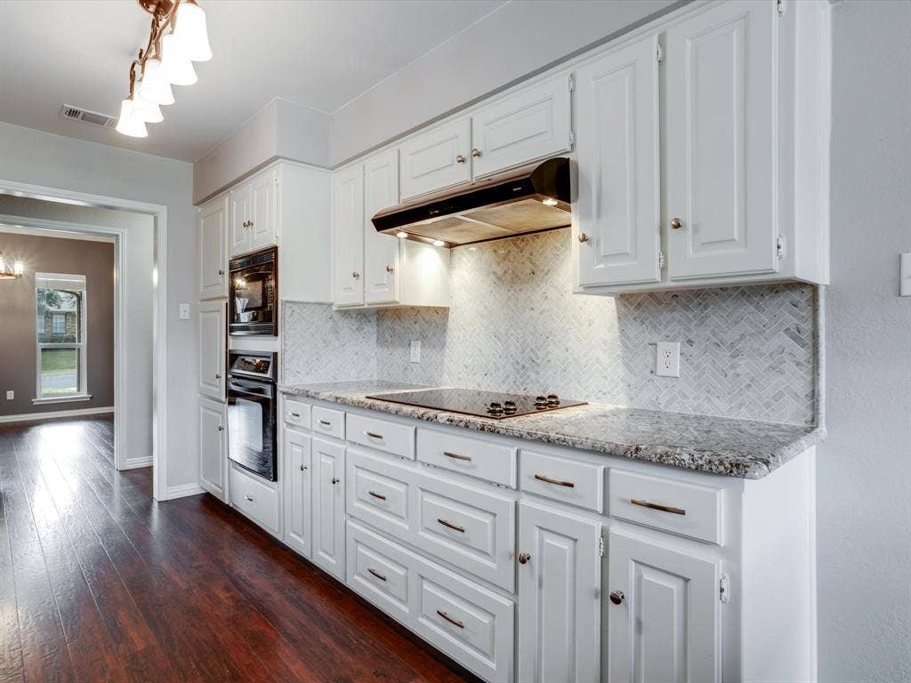 Kitchen featuring white cabinetry, stone-surface countertops, herringbone-pattern tile backsplash, built-in wall oven and microwave, and wood-finish flooring