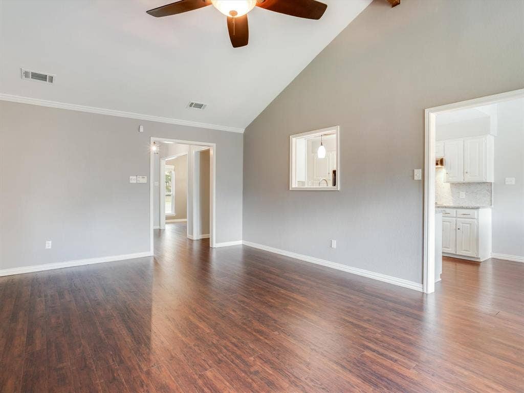 Vaulted ceiling with an integrated wooden-blade ceiling fan, wood-finish flooring, interior service window, and crisp neutral wall paint