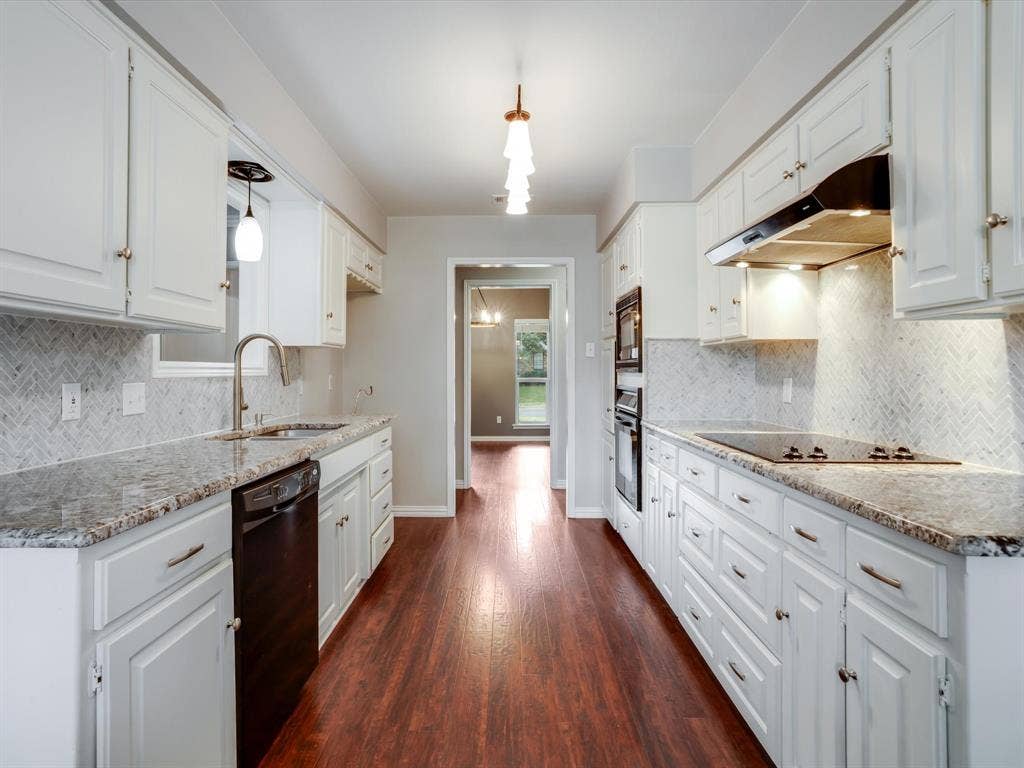 Kitchen featuring white cabinetry, stone countertops, herringbone-patterned backsplash, wood-finish flooring, and built-in stainless steel appliances