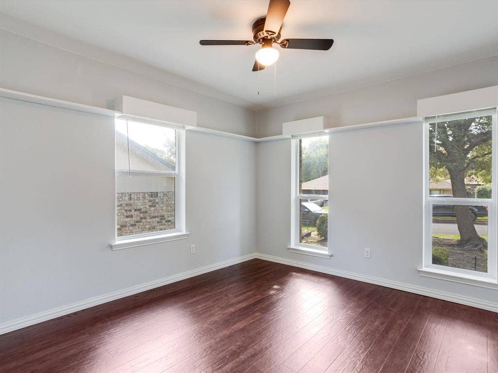 Interior space featuring dark wood-finish flooring, three windows with custom valances, and a ceiling-mounted light fixture with integrated fan