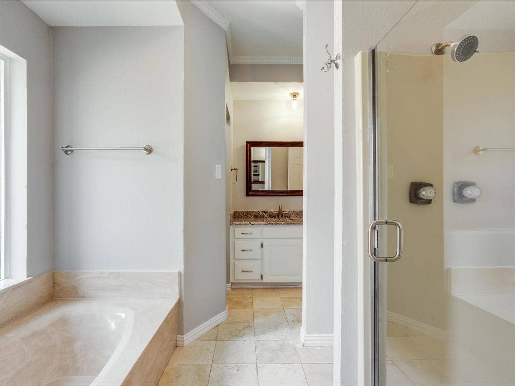 Soaking tub with stone-finish surround, frameless glass-enclosed shower, stone-topped vanity with undermount sink, and tile flooring
