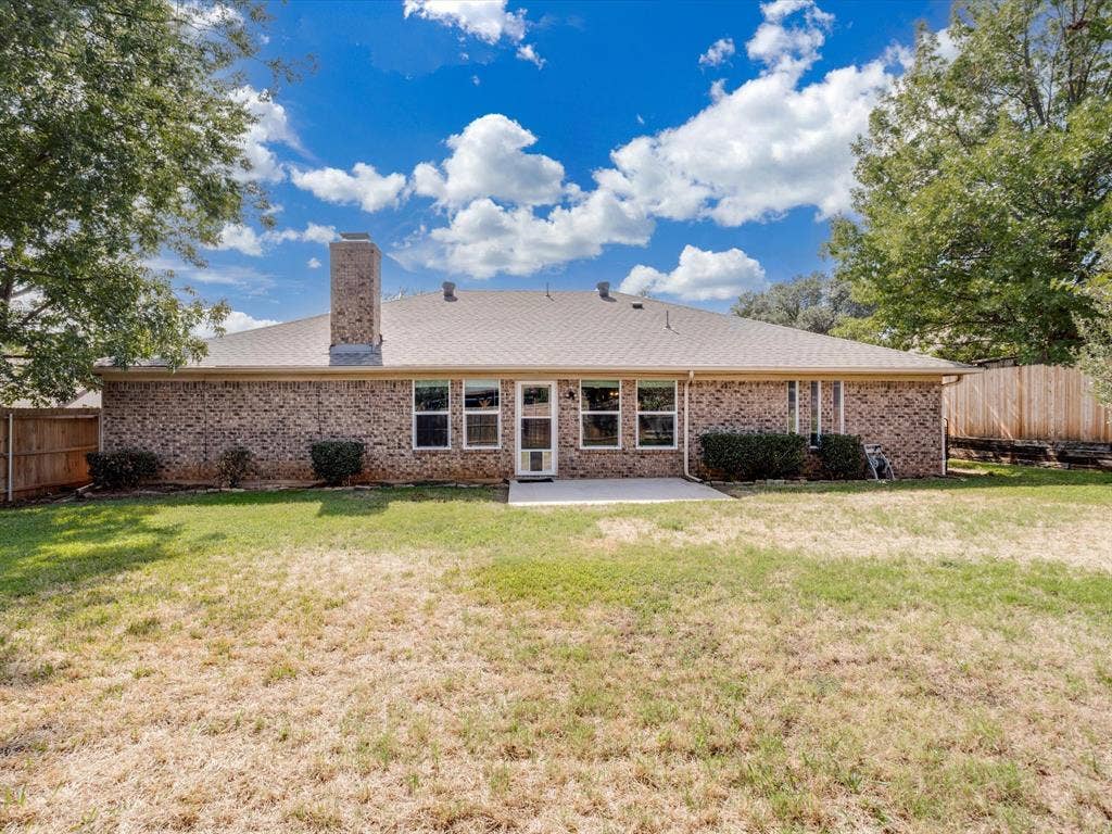 Rear exterior featuring a full brick facade, masonry chimney, concrete patio, and fenced backyard
