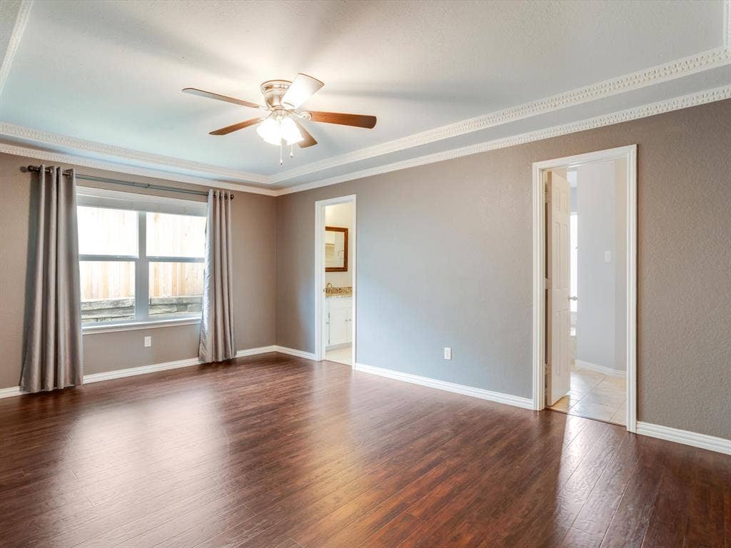 Tray ceiling with crown molding, wood-finish flooring, and a multi-blade ceiling fan with integrated lighting