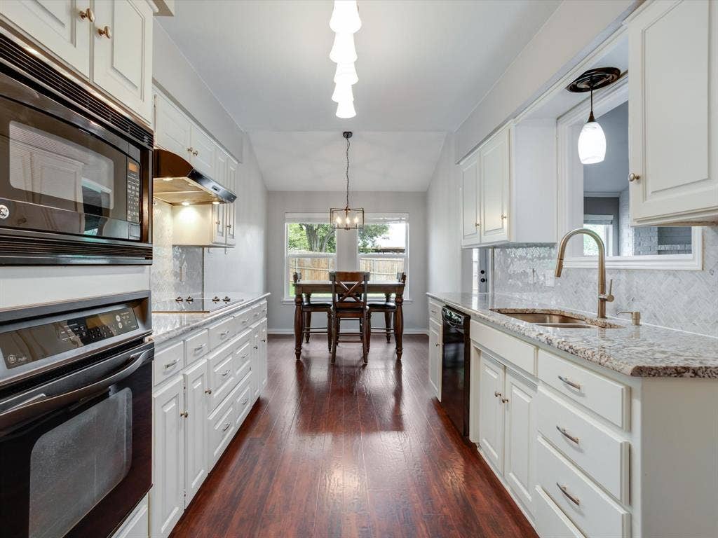 Kitchen featuring white shaker-style cabinetry, stone-finish countertops, wood-finish flooring, a herringbone-pattern tile backsplash, and built-in stainless steel appliances