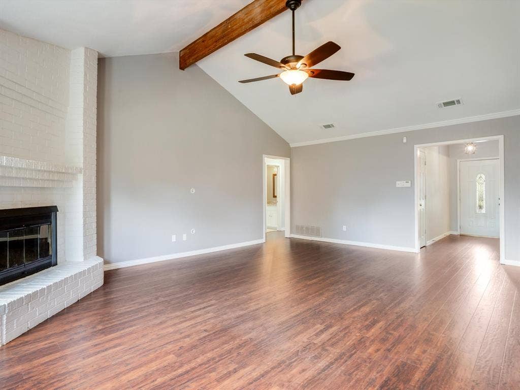 Vaulted ceiling featuring an exposed wood beam, wood-finish flooring, and floor-to-ceiling painted brick fireplace