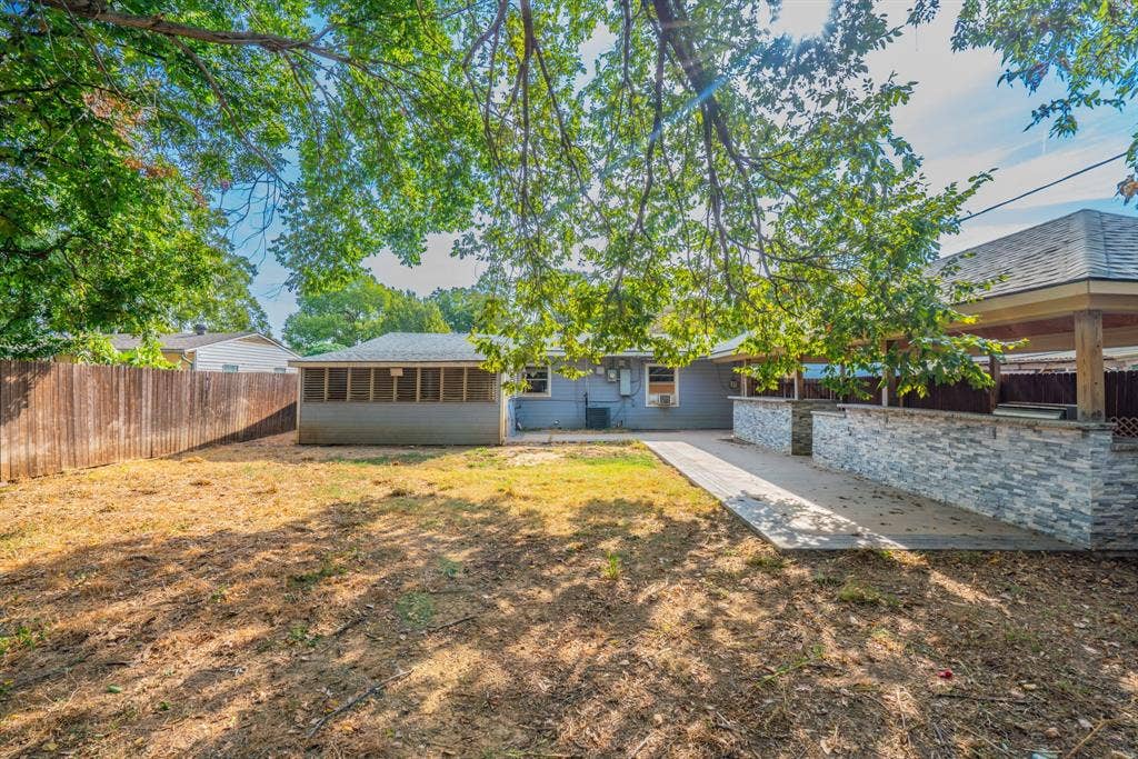 934 Indian Hills Drive, Grand Prairie, TX 75051 Expansive backyard featuring a privacy fence, covered patio with stone-veneer knee walls, and a screened-in porch
