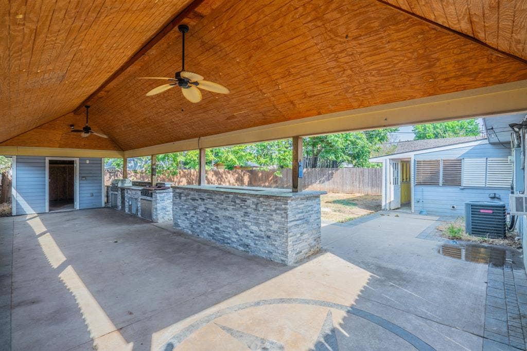 934 Indian Hills Drive, Grand Prairie, TX 75051 Expansive covered patio featuring a wood-finish ceiling, dual ceiling fans, and an outdoor kitchen with integrated appliances and a stone-clad bar