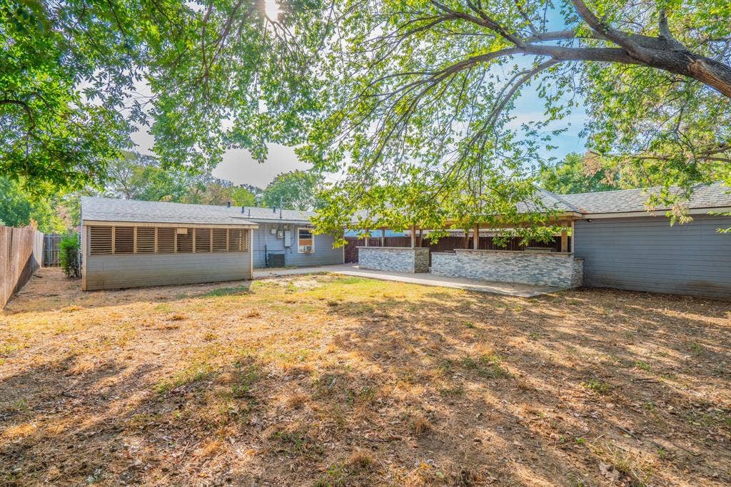 934 Indian Hills Drive, Grand Prairie, TX 75051 Expansive backyard featuring a screened-in porch, mature trees, and a stone-clad patio area