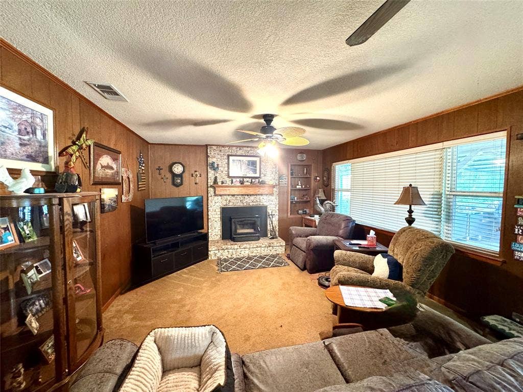 10122 Ash Cove, Wills Point, TX 75169 Brick-faced fireplace with a hearth insert, wood paneling, built-in shelving, ceiling fan, and carpeted flooring