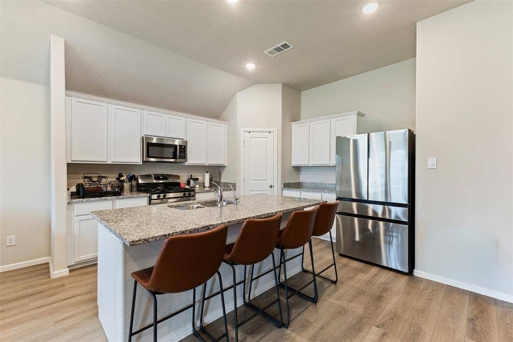 Kitchen with appliances with stainless steel finishes, white cabinetry, light stone counters, a breakfast bar, and a kitchen island with sink