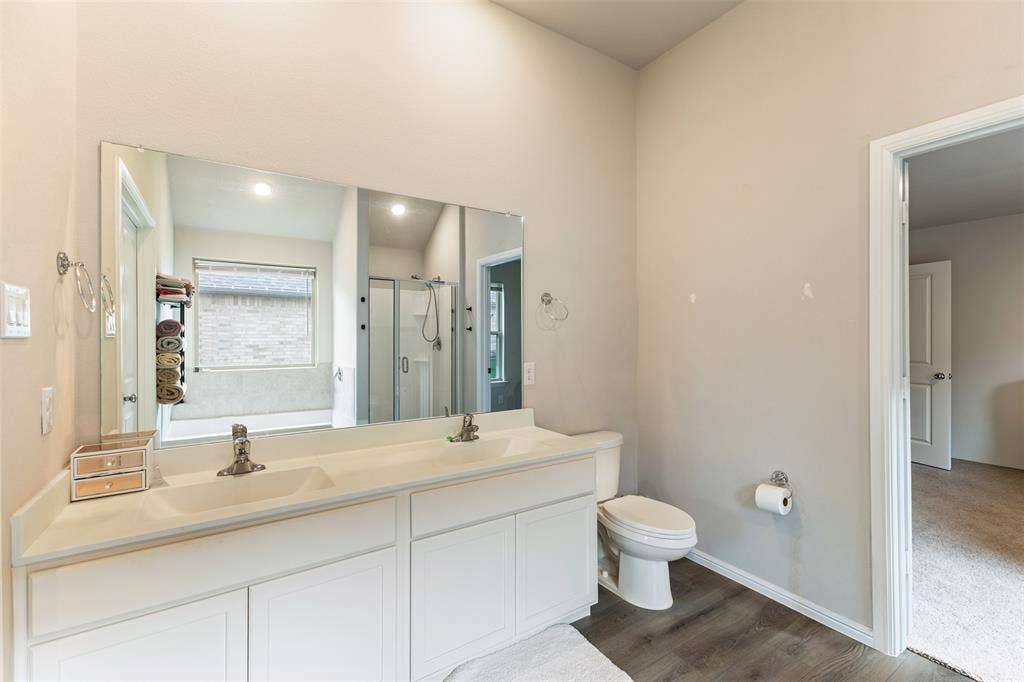 Bathroom featuring a garden tub, a shower stall, double vanity, and dark wood-style flooring