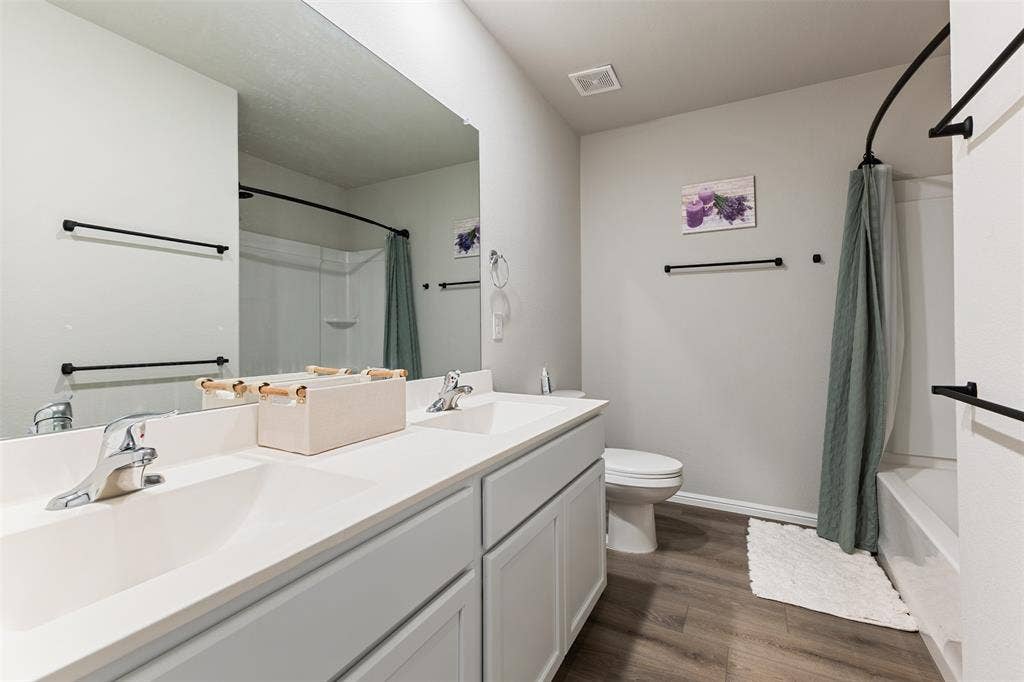 Bathroom featuring dark wood-type flooring, double vanity, and shower / bath combination with curtain