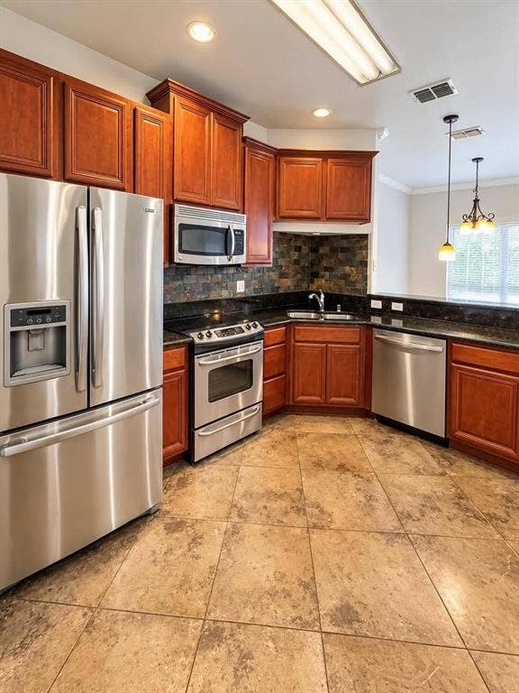 Kitchen featuring stainless steel appliances, dark stone countertops, natural wood-finish cabinetry, a coordinating stone backsplash, and neutral-toned tile flooring