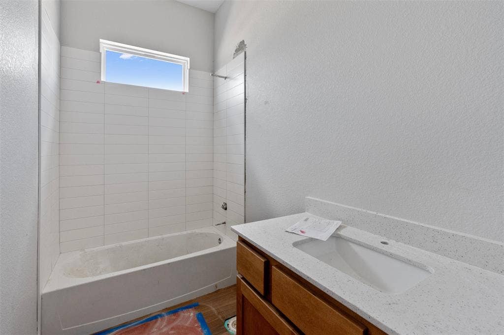 1312 Tahonta Drive, Hewitt, TX 76643 White subway tile shower surround, bathtub with integrated apron, horizontal window, wood-finish vanity with under-mount sink, speckled countertop