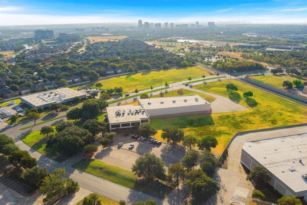 1701 W Walnut Hill Lane, #100, Irving, TX 75038 Aerial perspective showcasing multiple commercial buildings, extensive open land, and surrounding mature trees