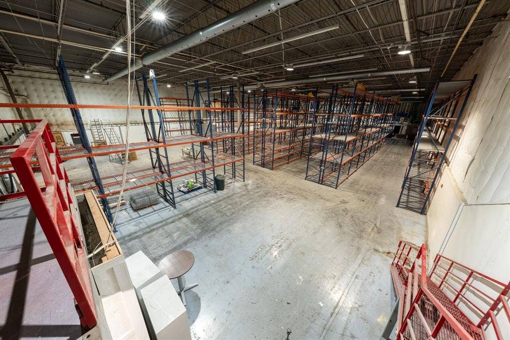 1701 W Walnut Hill Lane, #100, Irving, TX 75038 Warehouse space featuring exposed ceiling infrastructure, overhead lighting, concrete flooring, extensive pallet racking, and a red metal staircase