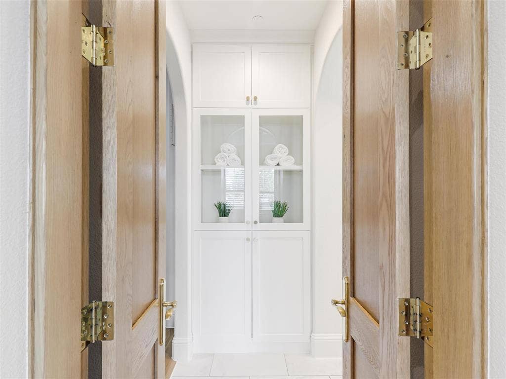 12313 Winding Hollow Lane, Frisco, TX 75033 Custom white oak double doors introduce a beautifully designed retreat that continues into a spa-inspired ensuite bath. High-end finishes include Fumo marble countertops, oversized custom mirrors, a generous 72-by-36-inch soaking tub, Delta faucets, rain shower, body spray jets, and tub faucet. The combination of natural stone, designer fixtures, and generous proportions creates the feeling of a private luxury spa within the home.Storage is equally impressive with a spacious 12-by-11-foot primary walk-in closet. Direct access from the primary suite area to the laundry room adds an exceptionally practical feature to the floor plan.