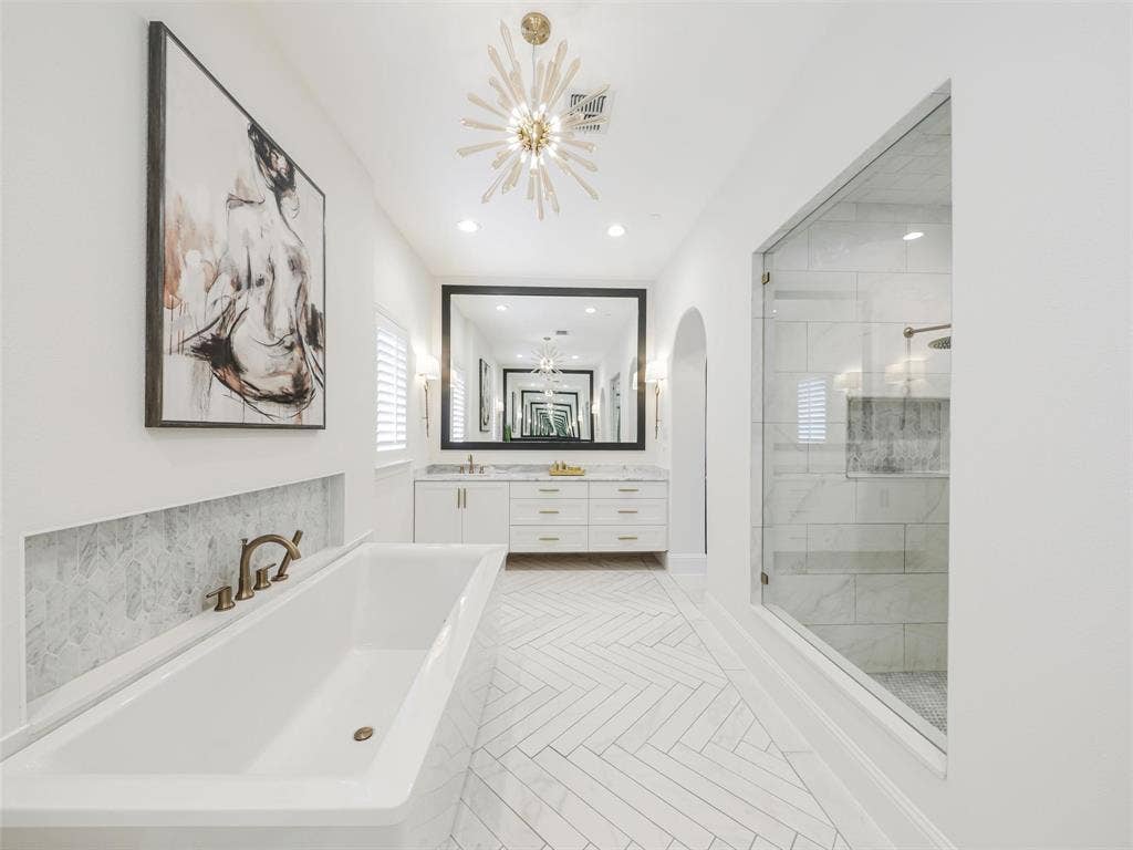 12313 Winding Hollow Lane, Frisco, TX 75033 Custom white oak double doors introduce a beautifully designed retreat that continues into a spa-inspired ensuite bath. High-end finishes include Fumo marble countertops, oversized custom mirrors, a generous 72-by-36-inch soaking tub, Delta faucets, rain shower, body spray jets, and tub faucet. The combination of natural stone, designer fixtures, and generous proportions creates the feeling of a private luxury spa within the home.Storage is equally impressive with a spacious 12-by-11-foot primary walk-in closet. Direct access from the primary suite area to the laundry room adds an exceptionally practical feature to the floor plan.