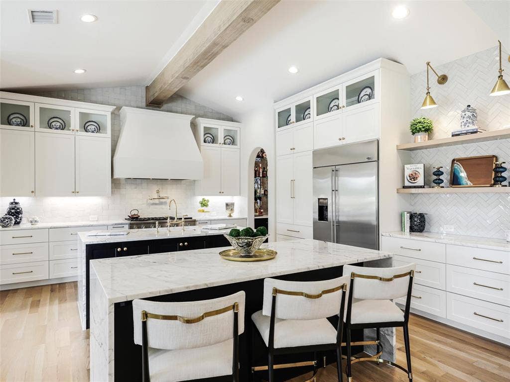 12313 Winding Hollow Lane, Frisco, TX 75033 Designed for both everyday living and large-scale entertaining, the chef-inspired kitchen serves as a stunning centerpiece of the home. Custom cabinetry provides extensive storage, while dual islands topped with beautiful White Arabescato marble offer generous preparation, serving, and gathering space. A U-Line 15-inch ice maker built into the second island adds another layer of convenience for entertaining. The kitchen is equipped with a premium GE Monogram appliance package and complemented by elegant Perrin & Rowe fixtures, creating a space where professional-quality functionality meets refined design.The adjoining butler’s pantry provides even more storage and preparation space with a butcher-block countertop, wine refrigerator, and dedicated appliance storage. Whether hosting an intimate dinner, holiday celebration, or a house full of guests, the kitchen and huge custom pantry were designed to keep entertaining organized while maintaining the clean, polished appearance of the main kitchen.