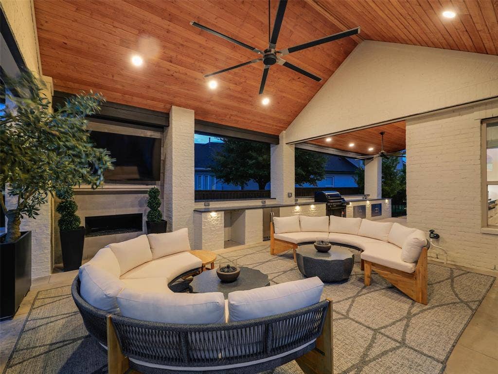 12313 Winding Hollow Lane, Frisco, TX 75033 Back Patio 9x28: The outdoor living center expands the entertaining possibilities even further with 9x28 of patio. A beautiful fireplace creates a natural focal point and allows the space to be enjoyed during cooler evenings, while a ceiling fan added in 2023 provides additional comfort during warmer months. The outdoor furnishings have been carefully selected to create multiple conversation areas and include two six-person half-moon sofas, area rugs, coffee tables, teak furniture, four rocking chairs, four rolling planters with trees, and decorative black metal privacy screens.
