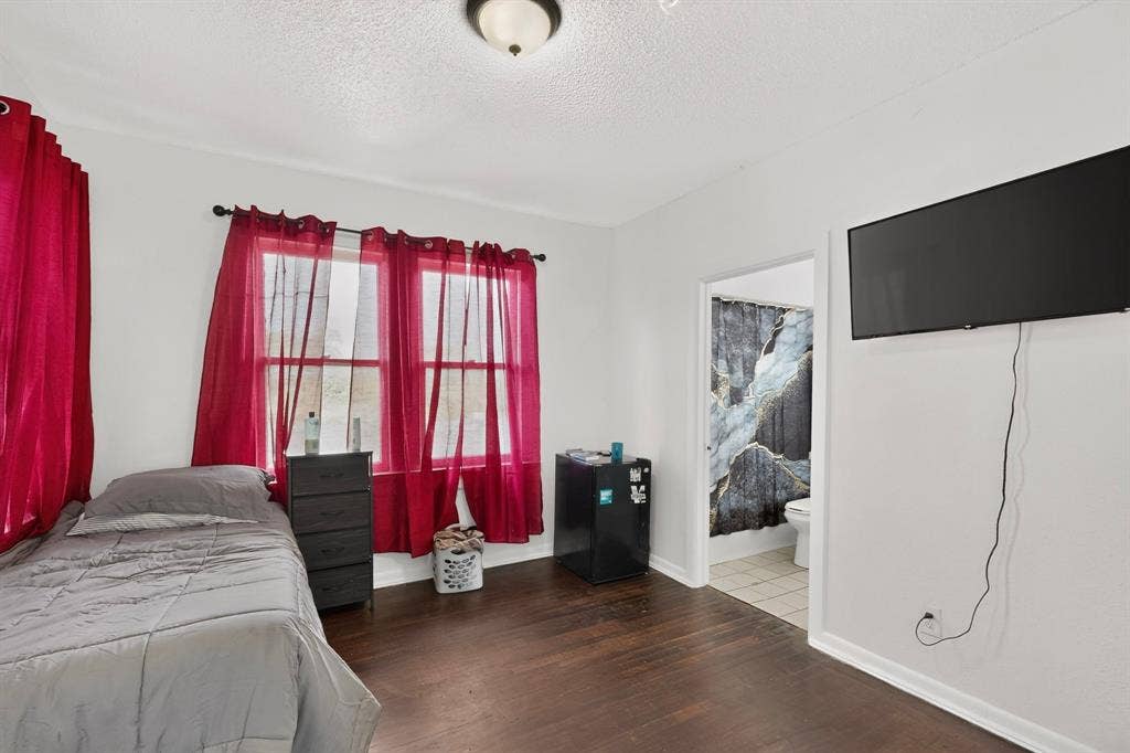 Hardwood-style flooring, white walls, two windows, ceiling-mounted light fixture, open doorway to an adjoining bathroom with tiled floor