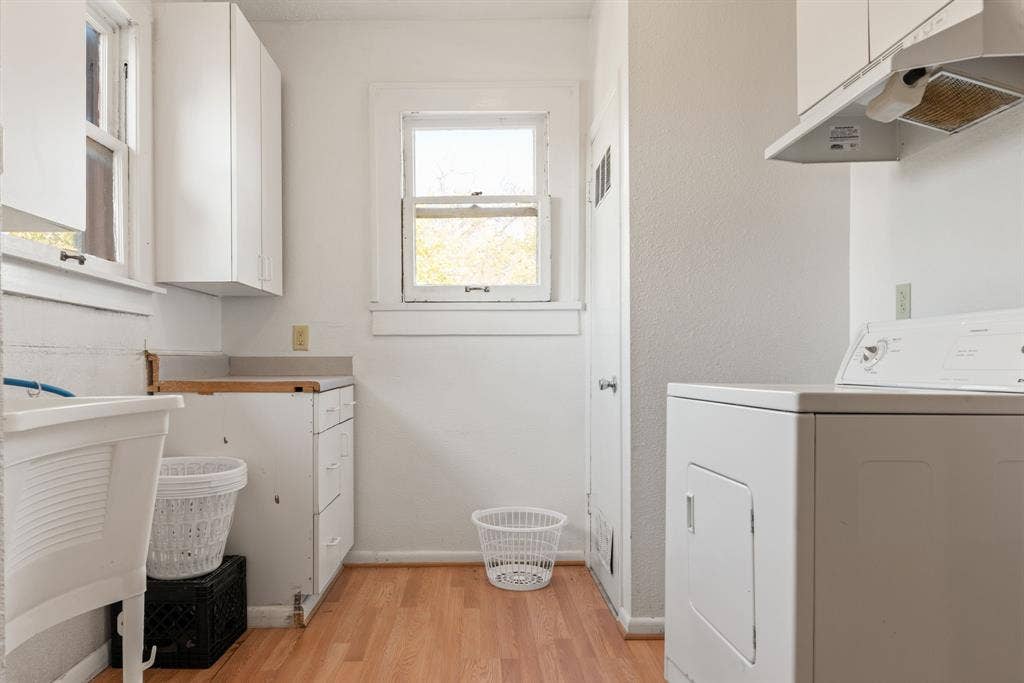 Wood-finish flooring with white walls, white cabinetry, and a utility sink