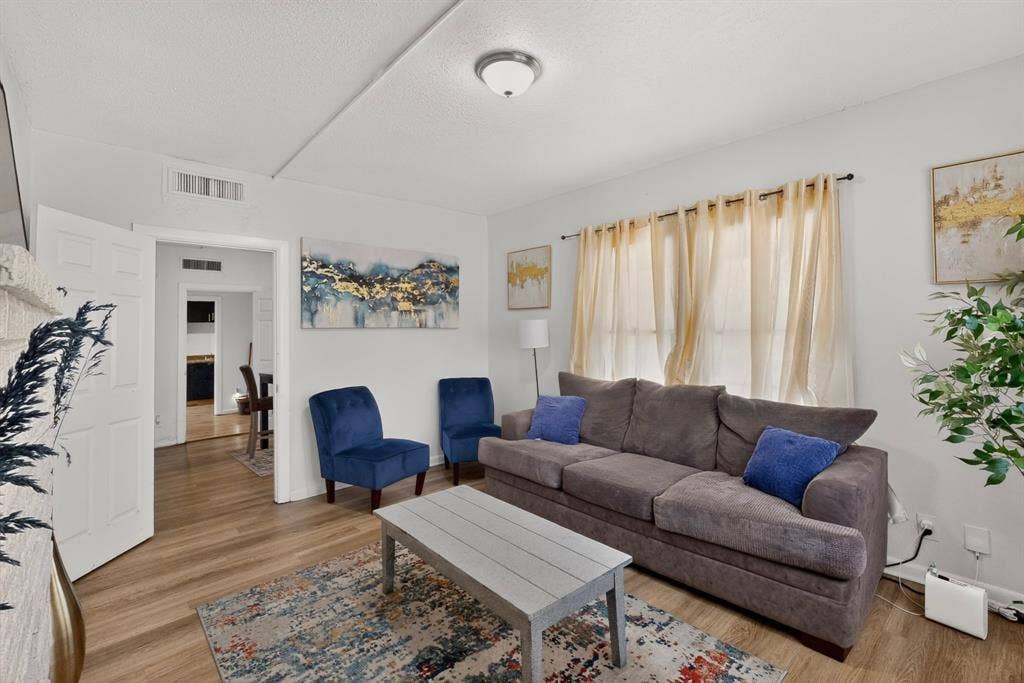 Wood-finish flooring throughout, white painted walls, and a window with curtain rod and drapes