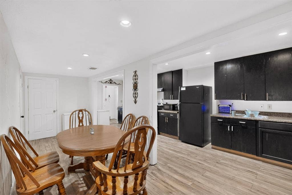 Open-concept kitchen and dining area featuring dark cabinetry, recessed lighting, and wood-finish flooring