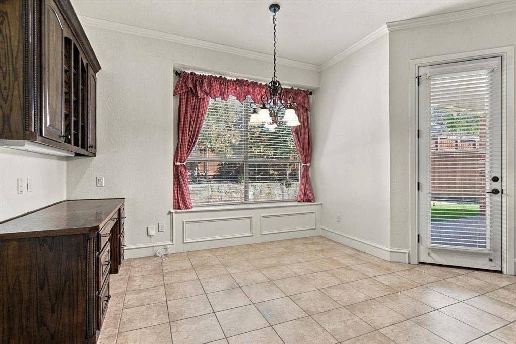 7004 Cherrybark Lane, North Richland Hills, TX 76182 Built-in dark wood cabinetry with integrated wine rack, neutral tile flooring, window with decorative trim, and crown molding