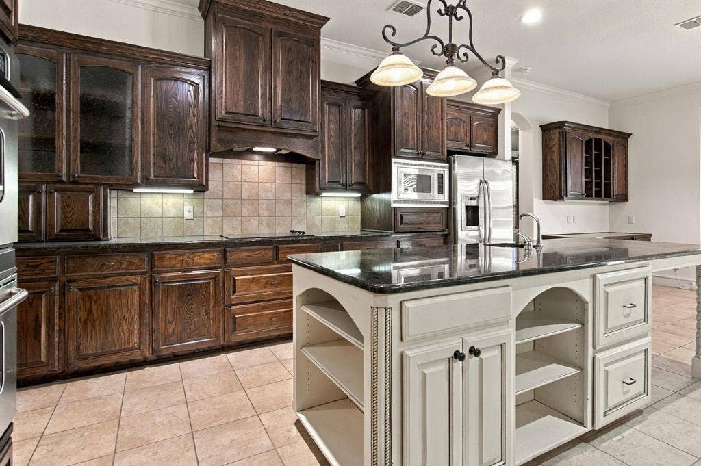 7004 Cherrybark Lane, North Richland Hills, TX 76182 Kitchen featuring dark wood cabinetry, a central island with integrated shelving, dark countertops, stainless steel appliances, and tile flooring