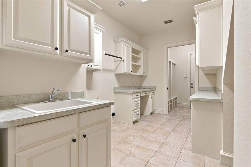 7004 Cherrybark Lane, North Richland Hills, TX 76182 Utility room featuring white cabinetry, a built-in sink with a countertop, tiled flooring, and a dedicated desk area