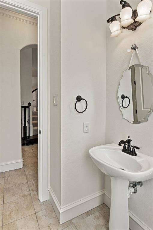 7004 Cherrybark Lane, North Richland Hills, TX 76182 Pedestal sink with black-finish faucet, decorative wall mirror, three-light vanity fixture, and tiled flooring