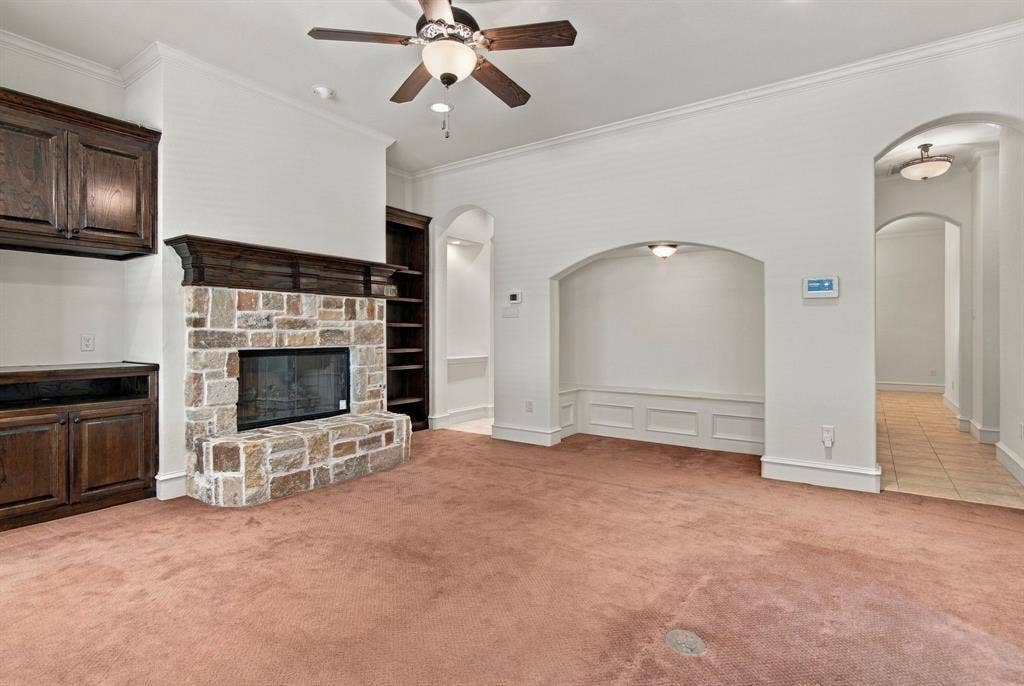 7004 Cherrybark Lane, North Richland Hills, TX 76182 Stone-faced fireplace with a wood mantle, built-in cabinetry, arched wall alcove, and ceiling fan