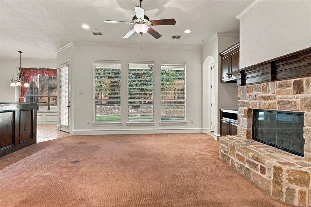 7004 Cherrybark Lane, North Richland Hills, TX 76182 Stone-clad fireplace with dark wood mantel, ceiling fan with integrated lighting, recessed lighting, multiple windows with horizontal blinds, and built-in wood cabinetry