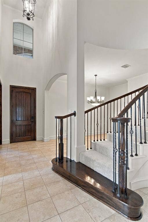 7004 Cherrybark Lane, North Richland Hills, TX 76182 Foyer featuring high ceilings, arched doorway, tile flooring, and a grand staircase with dark wood newel posts and iron balusters