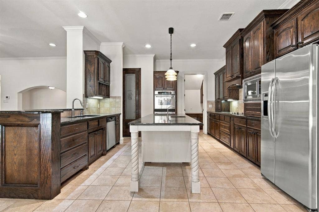 7004 Cherrybark Lane, North Richland Hills, TX 76182 Kitchen featuring dark wood cabinetry, stainless steel appliances, a center island with decorative legs, and tile flooring